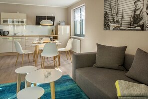 A modern kitchen with white cabinets, a dining area with a table and chairs, and a gray sofa in a living room. - House on the dike, harbor 3a H8 ground floor 48m² (Ostseebad Prerow)