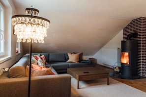 A cozy living room with a sectional sofa, a coffee table, a chandelier, and a wood-burning stove.