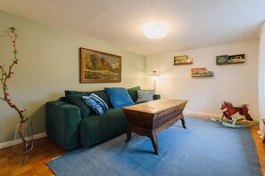 A living room with a green sofa, a wooden coffee table, a blue rug, a painting on the wall, and a small decorative tree.