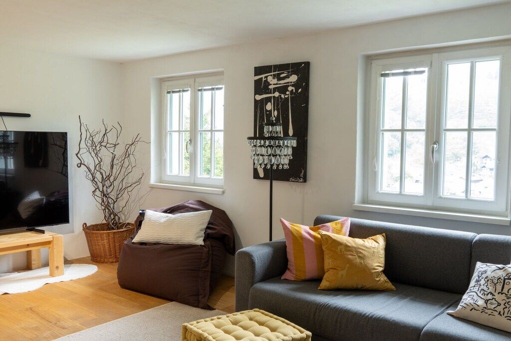 A living room with a grey sofa, a brown bean bag, a television, and a large abstract painting.