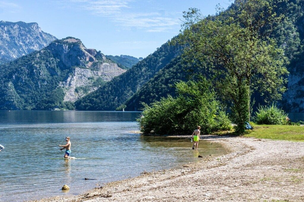 A lake with mountains in the background, a person wading in the water, and a tree-lined shore.