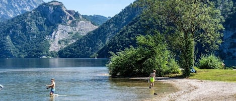 A lake with mountains in the background, a person wading in the water, and a tree-lined shore.