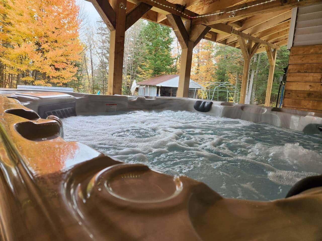 Un bain à remous avec une terrasse en bois et une vue sur les arbres aux couleurs automnales.