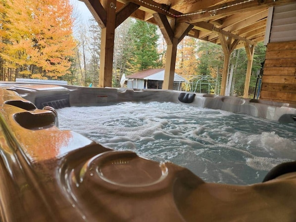 A hot tub with a wooden deck and a view of autumn trees.