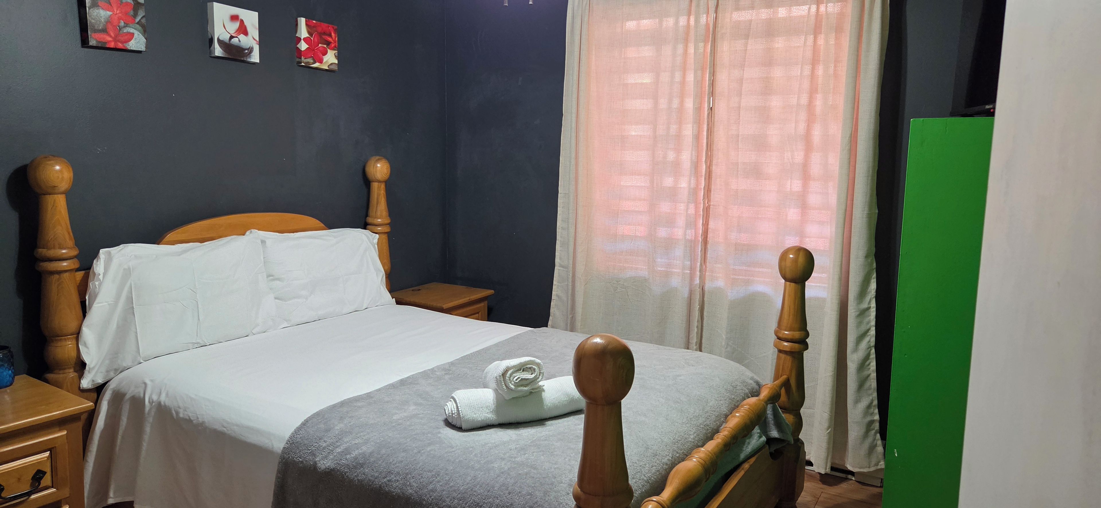 Une chambre à coucher avec un lit en bois, une table de chevet, une armoire verte et une fenêtre avec des rideaux.