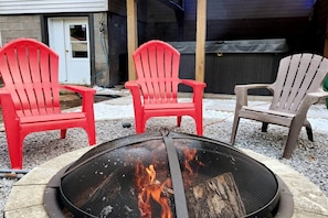 Un foyer extérieur entouré de trois chaises Adirondack, dont une rouge et deux grises, dans un jardin.