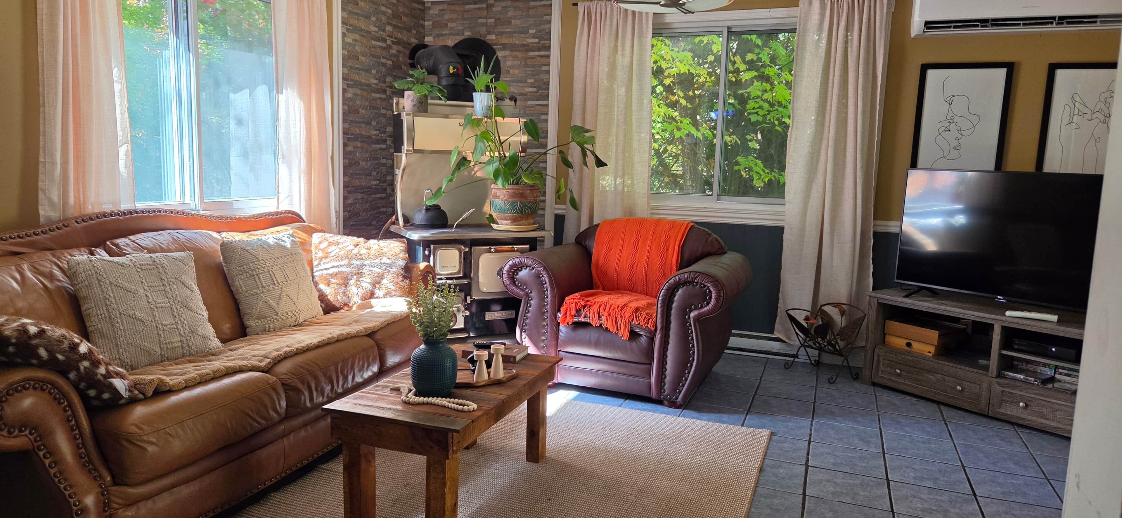 Un salon avec un canapé en cuir marron, une table basse en bois, un fauteuil rouge et un téléviseur.