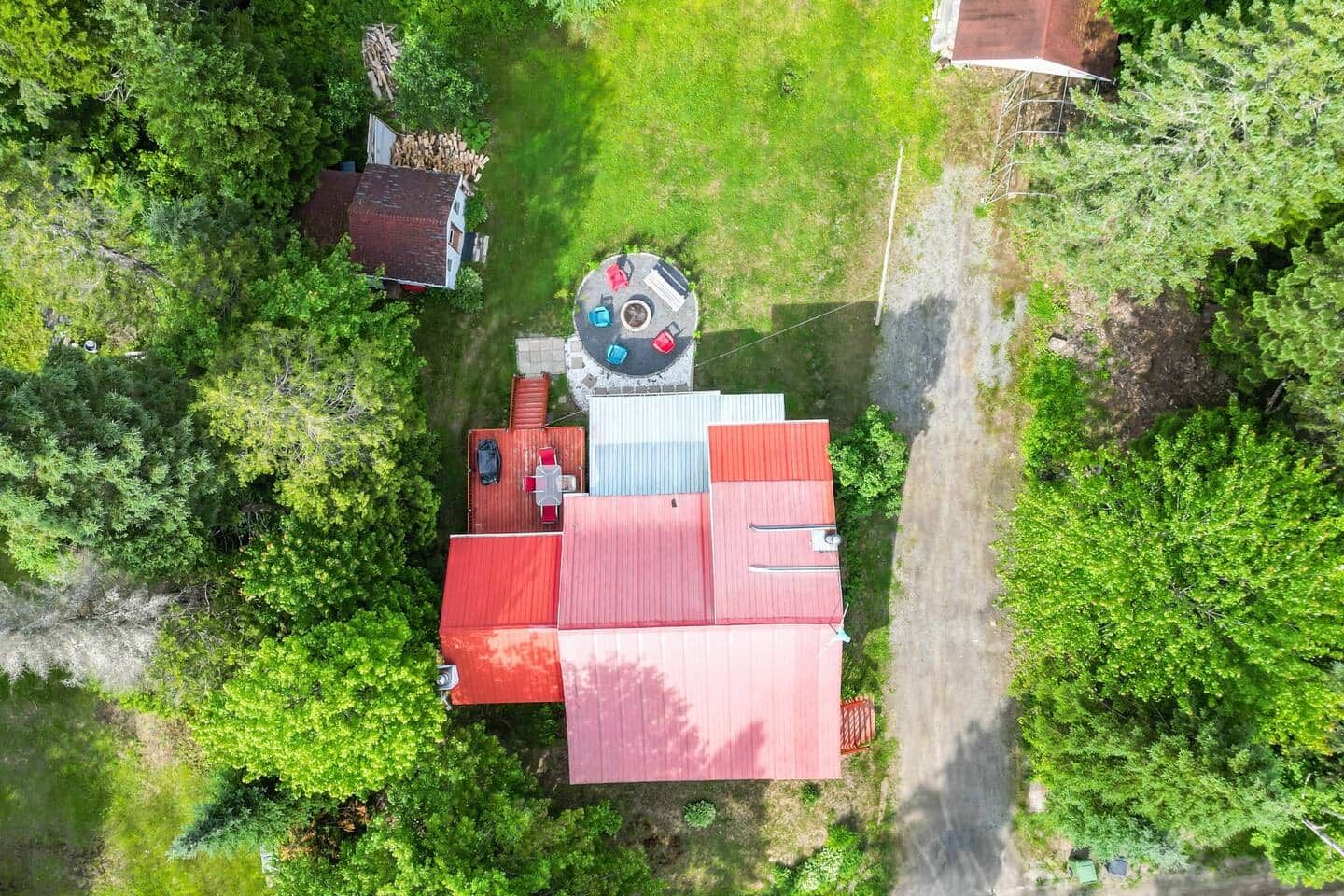 Vue aérienne d’une propriété comprenant un bâtiment à toit rouge, une petite terrasse et une végétation luxuriante.