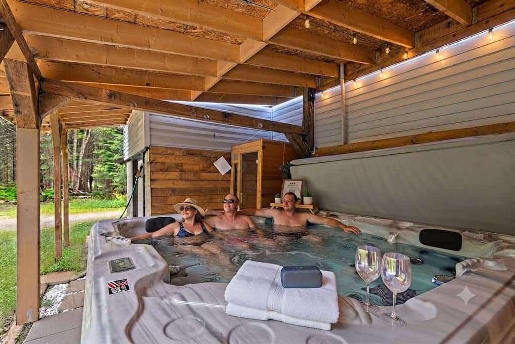 Un bain à remous avec une table et deux chaises, entouré de poutres en bois et abrité par une structure couverte.