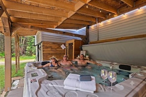 Un bain à remous avec une table et deux chaises, entouré de poutres en bois et abrité par une structure couverte.