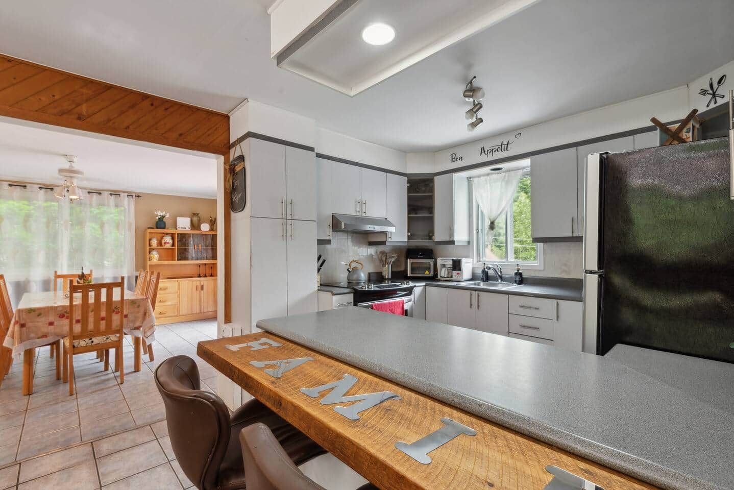 Une cuisine moderne avec un coin bar, un ensemble de salle à manger en bois et une vue sur l’extérieur.