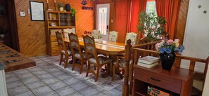 A wooden dining area with a table and chairs, a bookshelf, and a vase with flowers.