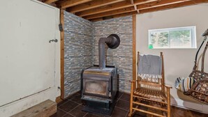 Quarto com parede de pedra, teto de madeira, fogão rústico, cadeira de vime e janela com vista.