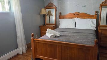Un letto di legno con un materasso grigio, due comodini con lampade, uno specchio e una finestra con tende.