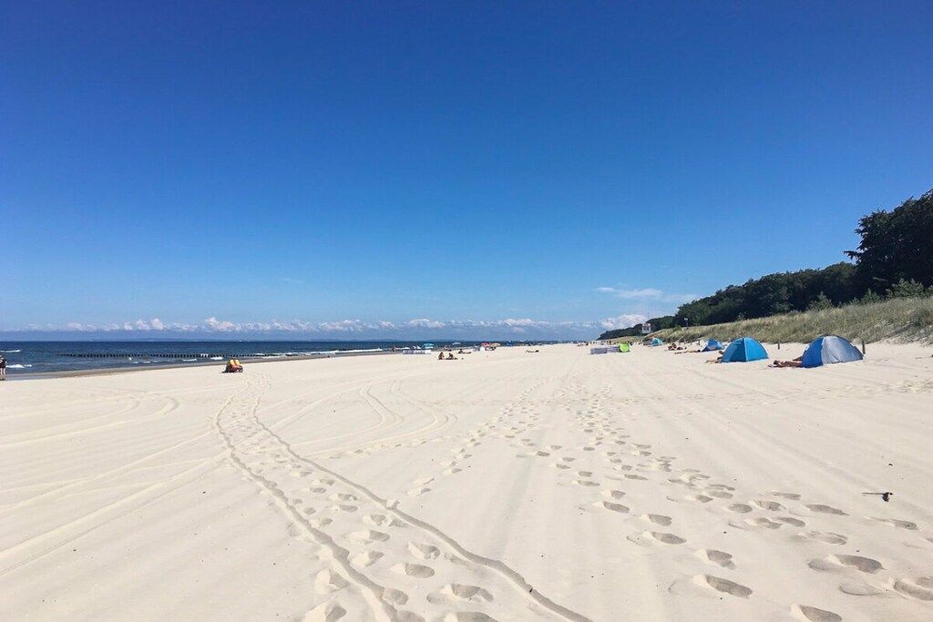 Une plage où l’on voit des empreintes de pas menant à l’eau, des tentes et un ciel dégagé.