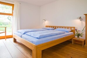 A wooden bed with a headboard, two bedside lamps, and a small bedside table with a vase of flowers. - Apple orchard Usedom (Reetzow)