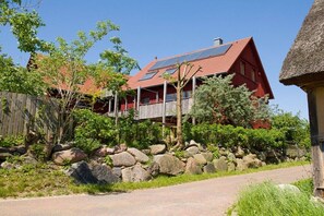 A red-roofed building with solar panels, surrounded by a wooden fence, rocks, and greenery. - Apple orchard Usedom (Reetzow)