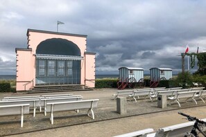 A beachside pavilion with a large arch entrance, a flag on top, and a row of benches. - Apple orchard Usedom (Reetzow)