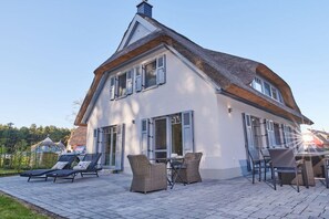 A two-story house with a sloped roof and shutters, a patio with outdoor furniture, and a clear sky. - Holiday home in Glowe with swimming pool (Glowe)