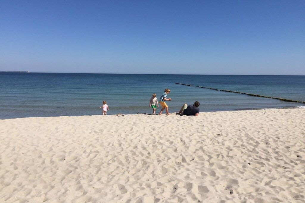 Een zandstrand met mensen, een heldere lucht en rustig water.