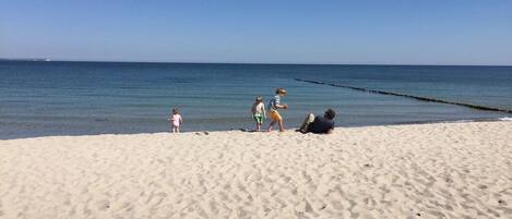 Een zandstrand met mensen, een heldere lucht en rustig water.