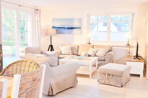 A modern living room with a sofa set, a coffee table, a wicker chair, and a side table with a lamp. - Holiday home in Glowe with swimming pool (Glowe)