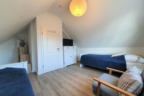A bedroom with a sloped ceiling, a bed with a dark blue bedspread, a bedside table with a lamp, and a chair with a striped cushion. - Holiday home in Prerow with swimming pool (Prerow)
