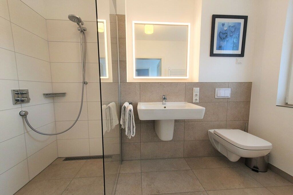 A modern bathroom with a glass-enclosed shower, a pedestal sink, and a toilet.