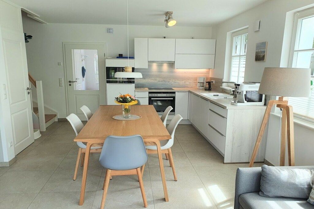 A modern kitchen with white cabinetry, a wooden dining table, and a built-in oven.
