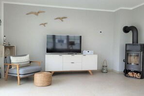 A modern living room with a flat-screen TV, white cabinetry, a grey sofa, a woven basket, and a wood-burning stove. - Holiday home in Prerow with swimming pool (Prerow)
