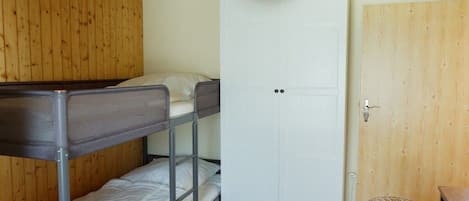 Una habitación con literas, una puerta blanca y una silla de mimbre.