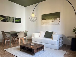 A living room with a sofa, coffee table, and a painting on the wall. - Bonaria: Apartment for 6 | Fiera, City Center, and Poetto (Cagliari)