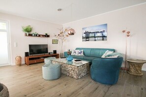 Una sala moderna con un sofá color turquesa, una mesa de centro de cristal y un televisor de pantalla plana.