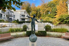 A statue of a figure on a pedestal in a landscaped area with benches and a building in the background. - Villa Louisa 43 - Octopussy (Ostseebad Sellin)