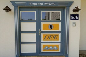 A blue door with the name 'Kapitan Parow' above it, a street sign 'No 33a' to the right, and a yellow sign with 'LEE' and a silhouette of a person. - Holiday apartment with 1 bedroom (Zingst)