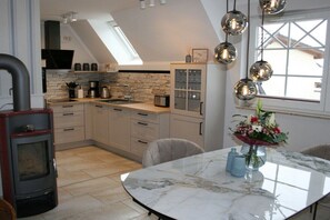 A modern kitchen with a stone backsplash, a built-in stove, and a dining area with a marble table. - Holiday apartment with 1 bedroom (Zingst)