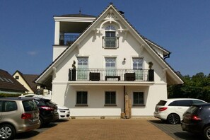 A two-story building with a balcony, a garage, and a parking area with cars. - Holiday apartment with 1 bedroom (Zingst)