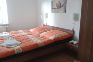A bed with an orange and white bedspread, two bedside lamps, and a nightstand with a device. - Holiday apartment on the edge of the forest (Eibenstock, OT Sosa)