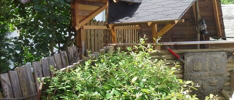 A wooden cabin with a sloped roof, surrounded by a wooden fence and dense foliage.