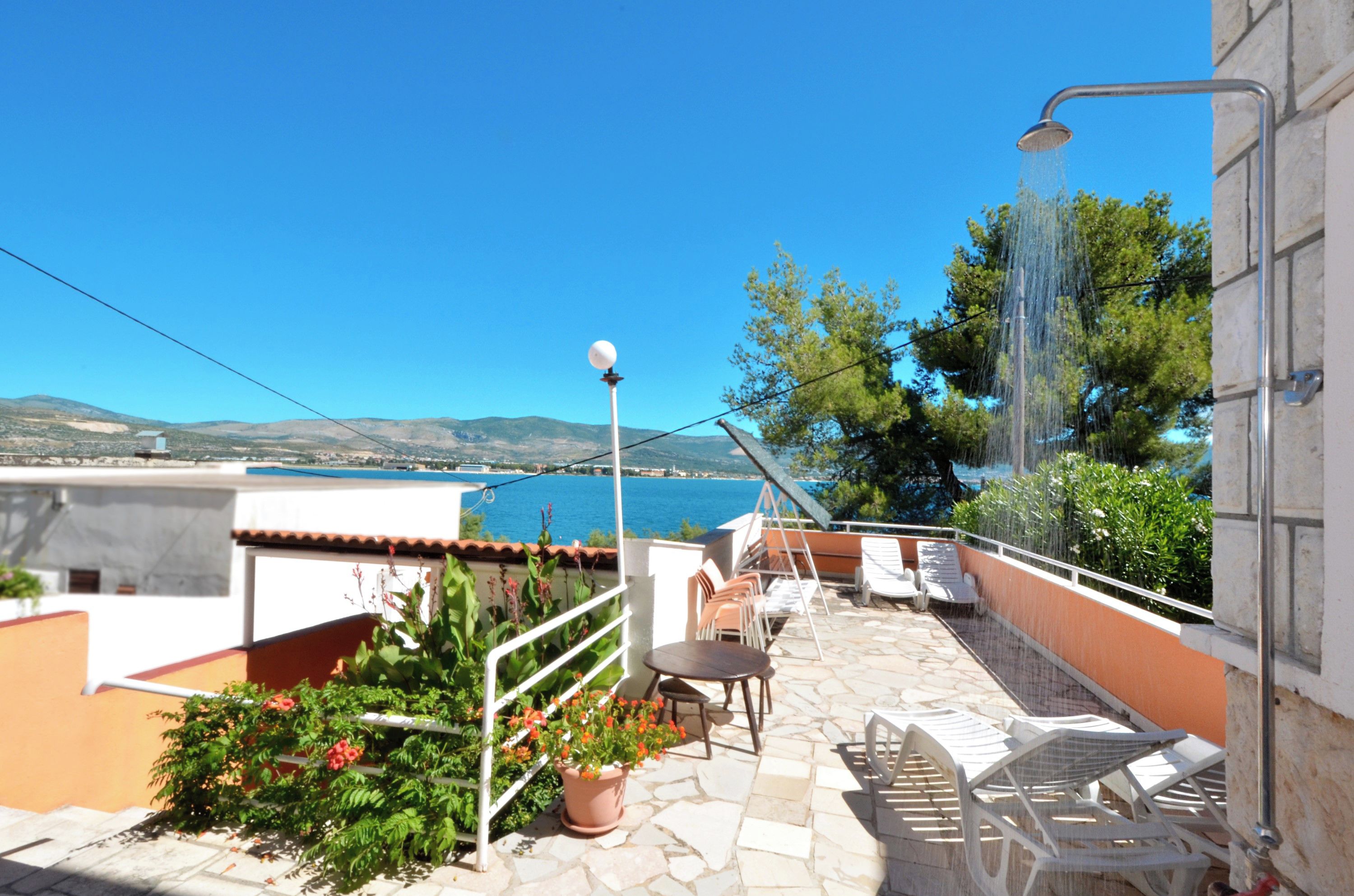 A rooftop terrace with a view of the sea, outdoor seating, and a water feature.