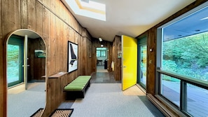 A hallway with wooden walls, a bench, and a large window with a view of trees.