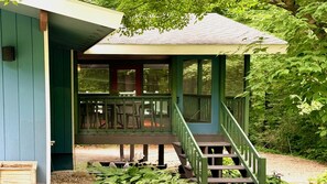 Une véranda en bois avec un escalier menant à une zone abritée, le tout entouré de verdure.