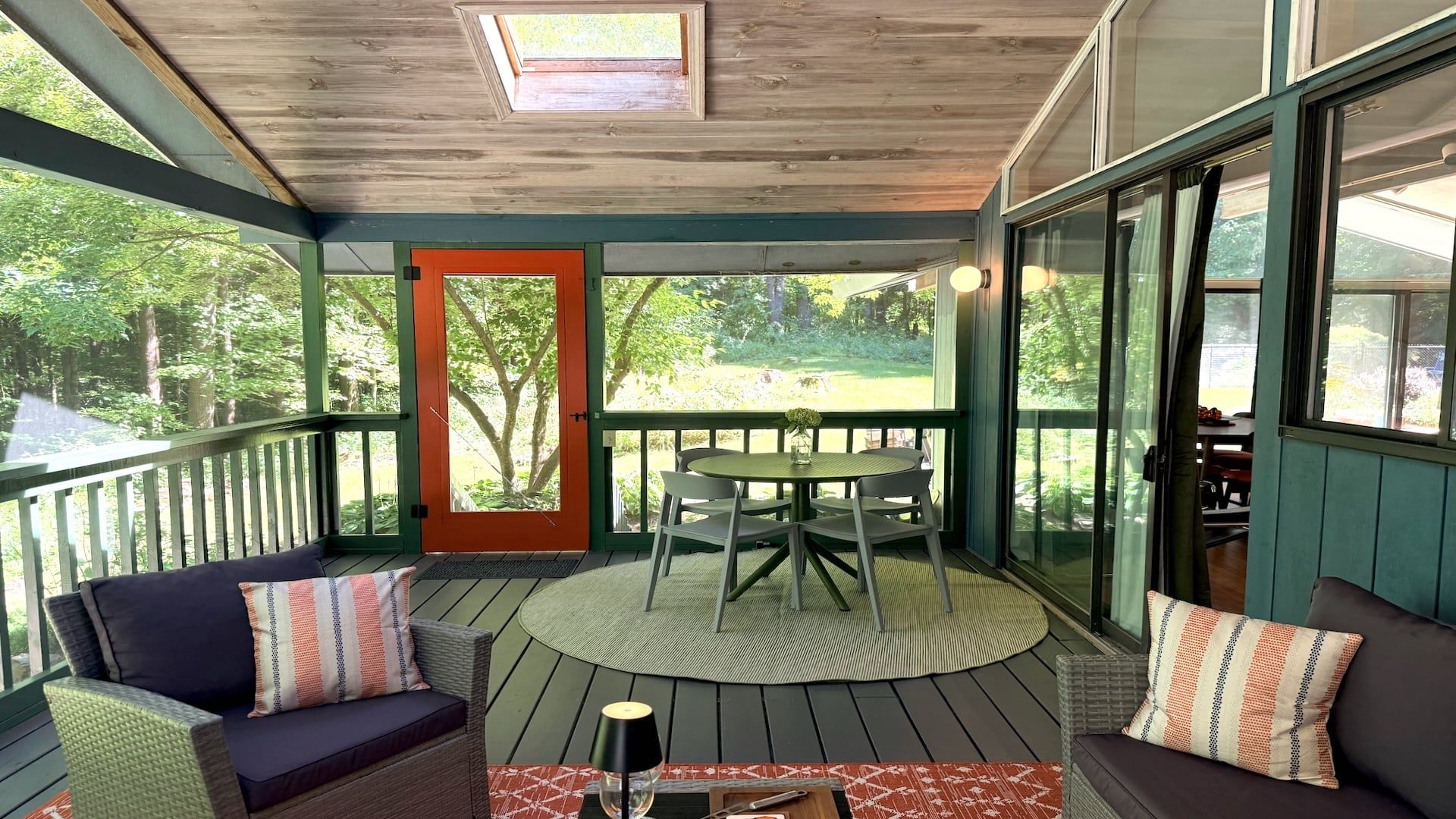 A covered porch with a table and chairs, a sofa, and a view of a green landscape.