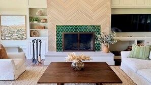 A living room with a fireplace, white sofas, a coffee table, and a TV.