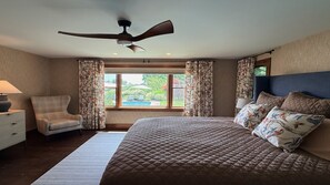 A bedroom with a bed, a chair, a desk, a ceiling fan, and a window with curtains.