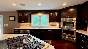 A modern kitchen with dark wood cabinets, stainless steel appliances, a central island with a gas stove, and a window providing natural light. - Mountain Views, Playroom, Fireplaces, Sleeps 8+! (Great Barrington)