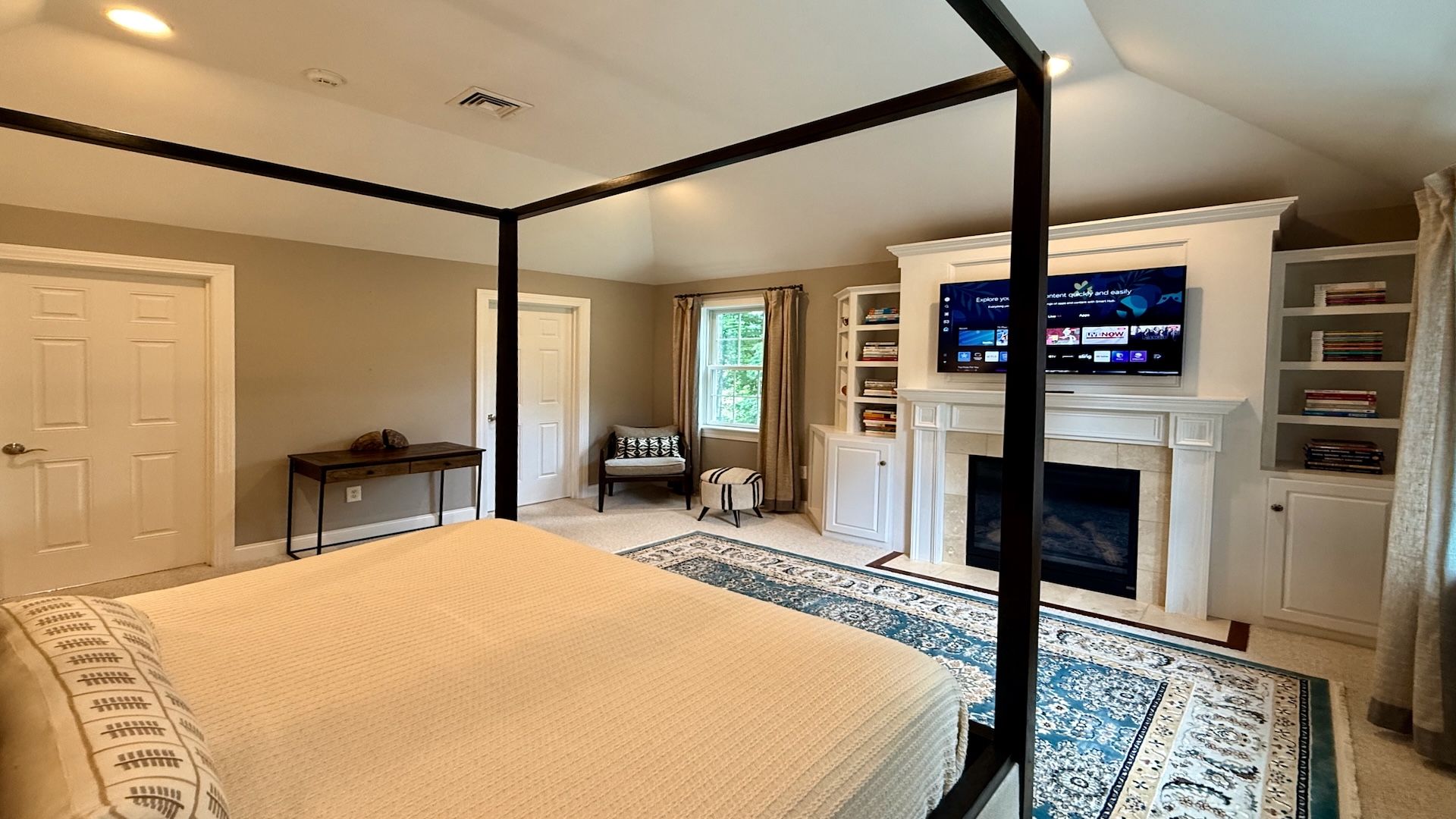 A bedroom with a four-poster bed, a fireplace, a television, and a bookshelf.