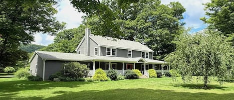A two-story house with a porch, surrounded by lush greenery and trees.