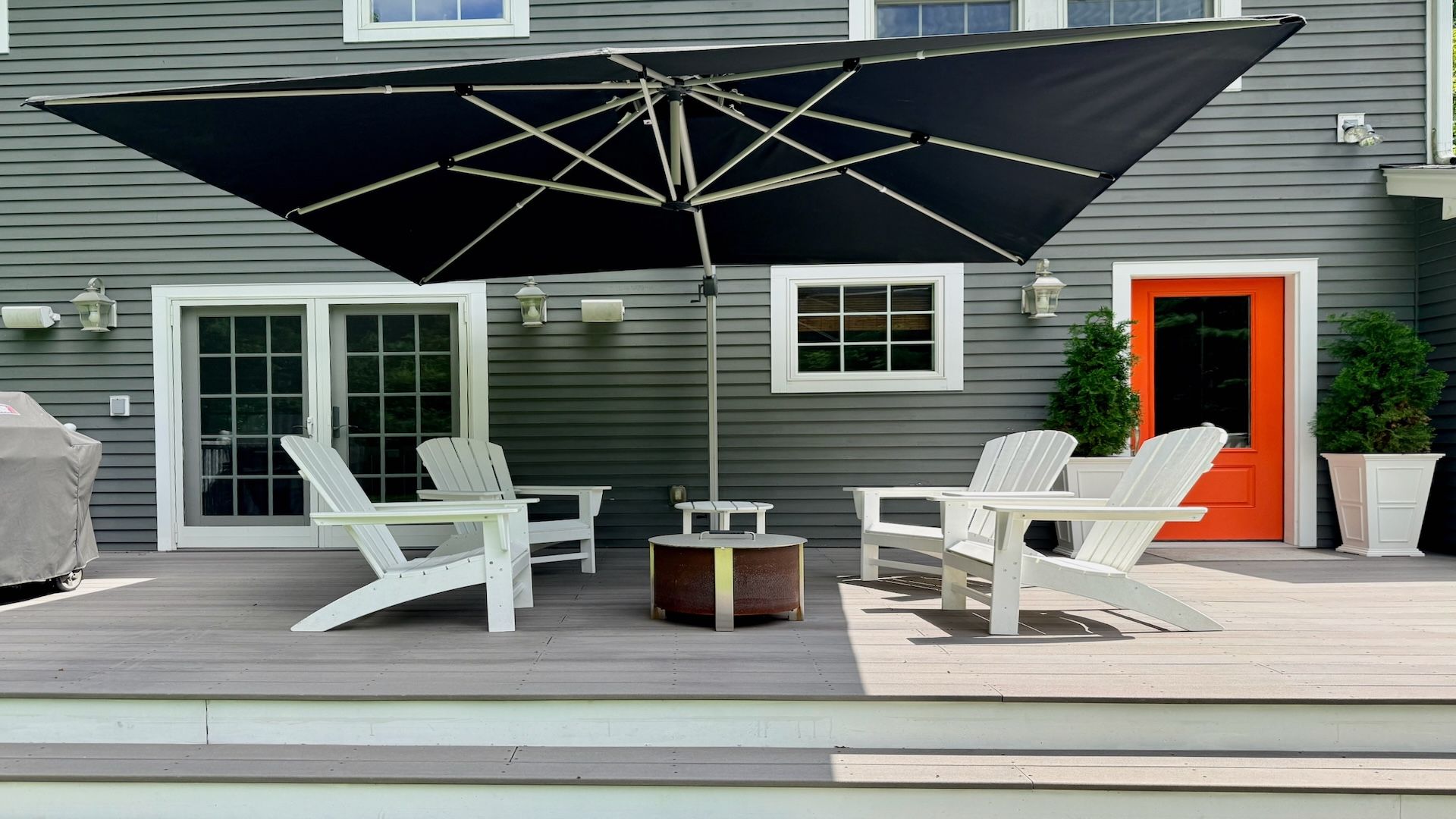An outdoor patio with a large umbrella, two Adirondack chairs, a round table, and a small potted plant.