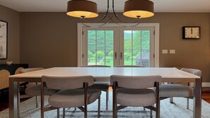 A dining room with a large table and six chairs, a chandelier, and a view of a green landscape through a glass door. - Mountain Views, Playroom, Fireplaces, Sleeps 8+! (Great Barrington)